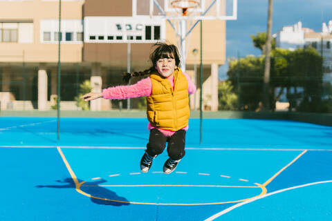 Cheerful girl jumping at sports court during sunny day stock photo