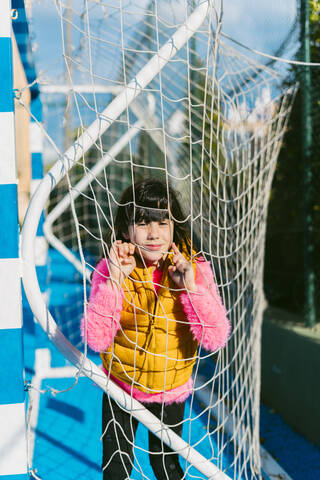Cute girl leaning on goal post net at soccer court during sunny day stock photo