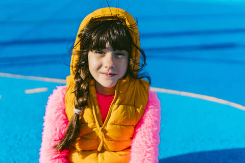 Cute girl in warm clothing sitting on sports court during sunny day stock photo