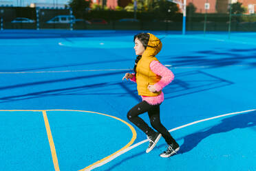 Mädchen läuft auf blauem Sportplatz während sonnigen Tag - ERRF04667