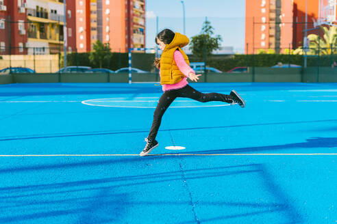 Mädchen springt auf blauem Sportplatz während sonnigen Tag - ERRF04672