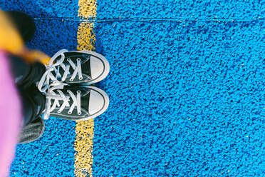 Girl standing on yellow line on blue sports court - ERRF04674