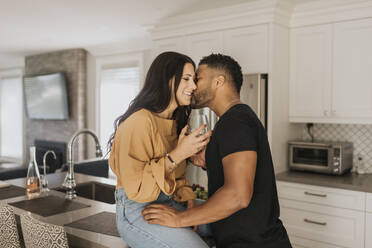 Man kissing woman sitting on kitchen counter at home - SMSF00374