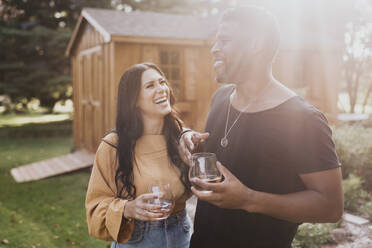 Glückliches Paar mit Weinglas, das lächelnd im Hinterhof steht - SMSF00379