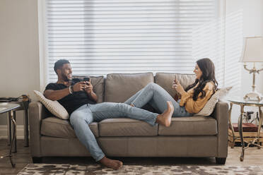 Couple using mobile phone while sitting on sofa at home - SMSF00387