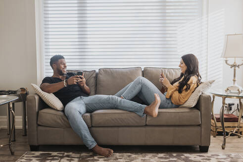 Ein Paar benutzt ein Mobiltelefon, während es zu Hause auf dem Sofa sitzt - SMSF00387