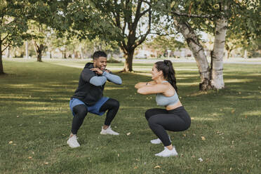 Smiling couple doing crouching exercise together while standing at backyard - SMSF00406