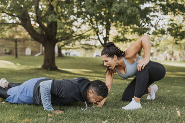 Woman motivating man doing push ups at backyard - SMSF00407