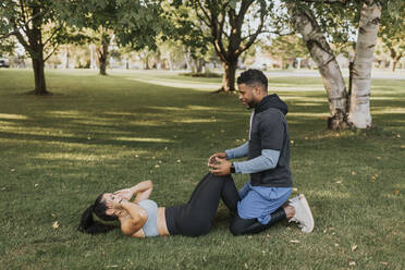 Mann hilft Frau bei Sit-ups im Sitzen auf Gras im Hinterhof - SMSF00409