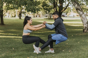 Couple holding hands while doing crouching exercise together at backyard - SMSF00413
