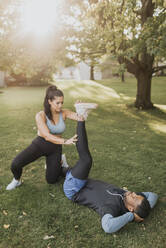 Woman helping man while stretching his legs while exercising at backyard - SMSF00415