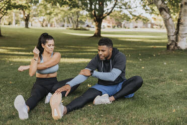 Couple doing warm up exercise while sitting on grass at backyard - SMSF00417