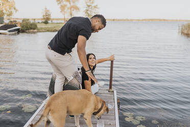 Mann steht mit Frau und Hund auf einem Steg am See - SMSF00437