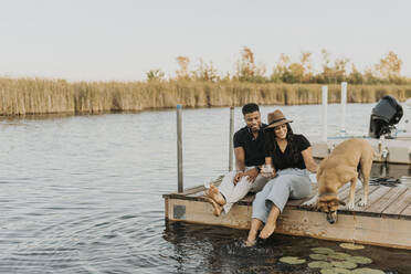 Smiling couple sitting with dog on pier - SMSF00444