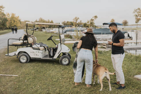 Paar mit Hund steht neben Golfwagen im Freien - SMSF00451