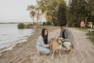 Pärchen schaut Hund an, während es bei Sonnenuntergang am See kauert - SMSF00466