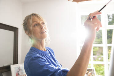 Ältere Frau malt zu Hause an einem sonnigen Tag - PMF01485