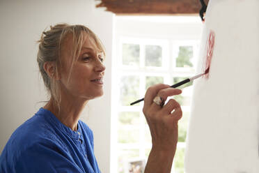 Aktive ältere Frau, die sich beim Malen auf einer Leinwand zu Hause konzentriert - PMF01486