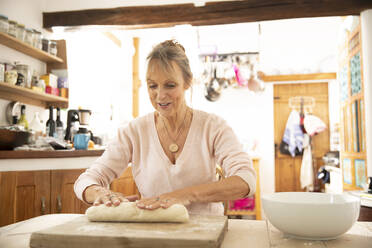 Ältere Frau bereitet Teig vor, während sie in der Küche sitzt - PMF01498