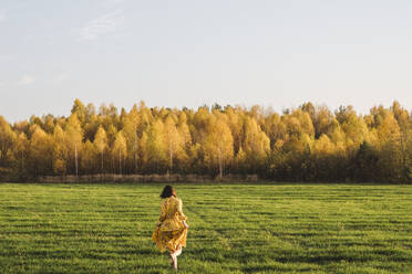 Mid adult woman walking on grass in autumn field on sunny day - EYAF01380