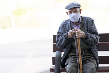 Senior man wearing protective face mask sitting on bench outdoors - GGGF00016