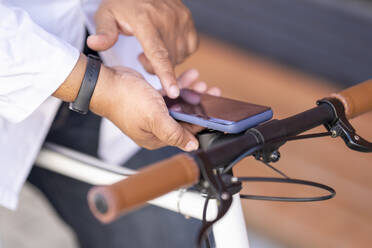 Nahaufnahme eines Mannes, der ein Smartphone benutzt, während er auf einem Fahrrad sitzt - GGGF00029