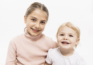 Smiling sisters sitting against white background in studio - DHEF00496