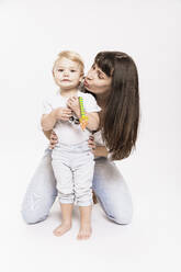 Mother embracing daughter from back while kneeling in studio against white background - DHEF00498