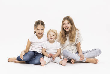 Lächelnde Schwestern sitzen mit gekreuzten Beinen vor weißem Hintergrund im Studio - DHEF00508