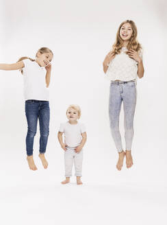 Schwestern springen vor weißem Hintergrund im Studio - DHEF00510