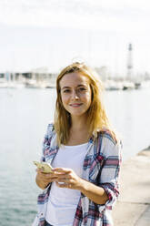 Woman using smart phone standing at seaside - XLGF00668