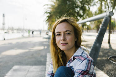 Young woman sitting on footpath during sunny day - XLGF00670