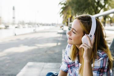 Junge Frau hört Musik über Kopfhörer auf einem Fußweg an einem sonnigen Tag - XLGF00674
