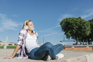 Frau hört Musik, während sie an einem sonnigen Tag auf dem Fußweg sitzt - XLGF00678