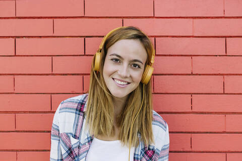 Smiling woman listening to music through headphone against brick wall stock photo