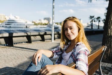 Junge Frau sitzt auf einer Bank an einem sonnigen Tag - XLGF00701