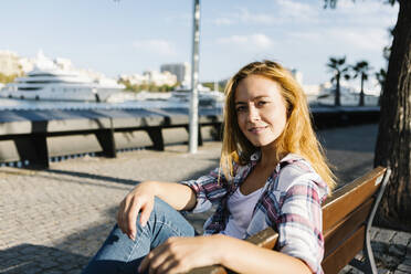 Young woman sitting on bench during sunny day - XLGF00701