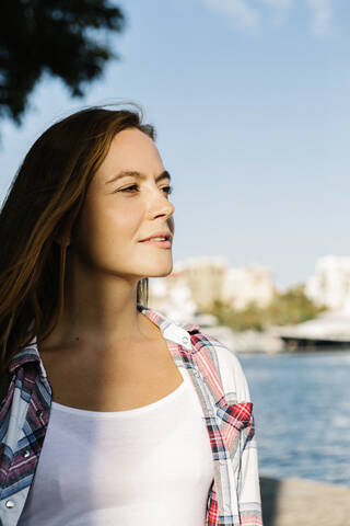 Thoughtful woman looking away while standing at seaside on sunny day stock photo