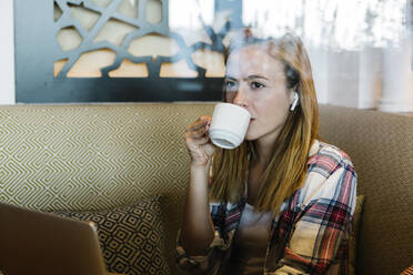 Woman looking away while drinking coffee sitting at home - XLGF00713