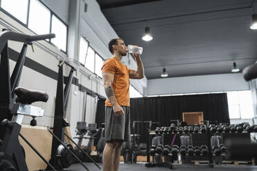 Mid adult man drinking water while standing in gym - SNF00699