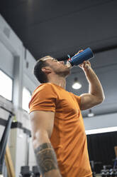 Durstiger Mann trinkt Wasser, während er im Fitnessstudio steht - SNF00700
