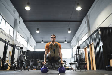 Männlicher Sportler beim Training mit einer Kesselglocke im Fitnessstudio - SNF00705