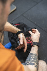 Male athlete wrapping sports glove while sitting in gym - SNF00711