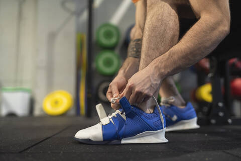 Male athlete tying shoelace while sitting in gym stock photo