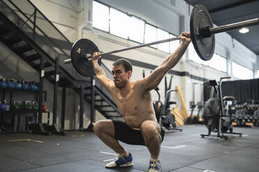 Sportler in der Hocke beim Aufheben einer Langhantel im Fitnessstudio - SNF00720