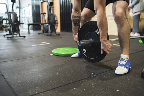 Mann hebt eine Langhantel auf, während er im Fitnessstudio steht - SNF00721