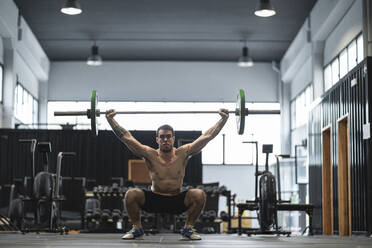 Männlicher Sportler in der Hocke beim Heben einer Langhantel im Fitnessstudio - SNF00724