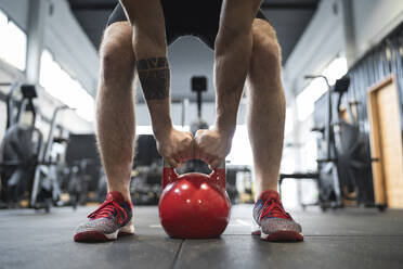 Beine eines männlichen Sportlers, der eine Kettlebell hält, während er im Fitnessstudio steht - SNF00727