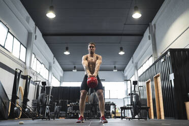 Männlicher Sportler, der eine Kettlebell aufhebt, während er im Fitnessraum steht - SNF00730