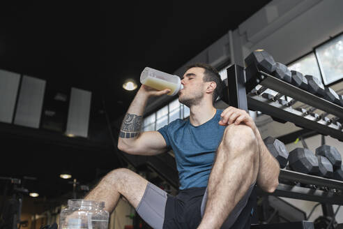 Male athlete drinking protein shake while sitting in gym - SNF00738